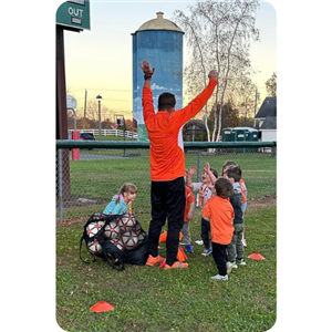 Soccer Coach in bright orange shirt celebrating with small children after practice ended
